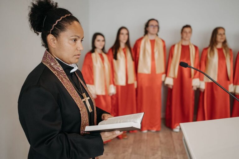 Choir leader holds an open hymnal before singers in red robes