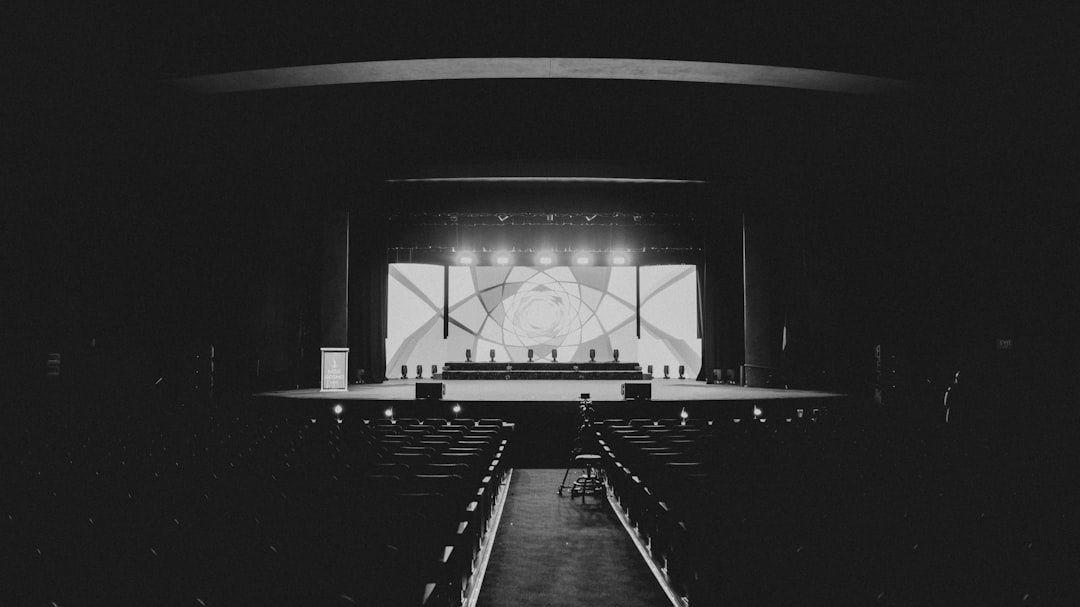 Black-and-white auditorium with a brightly lit stage and empty seats