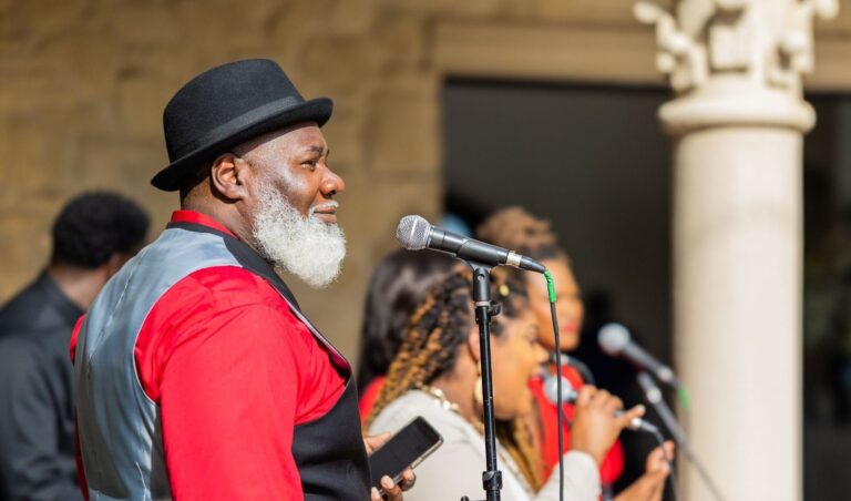 Gospel singer in a hat faces a microphone with musicians behind him